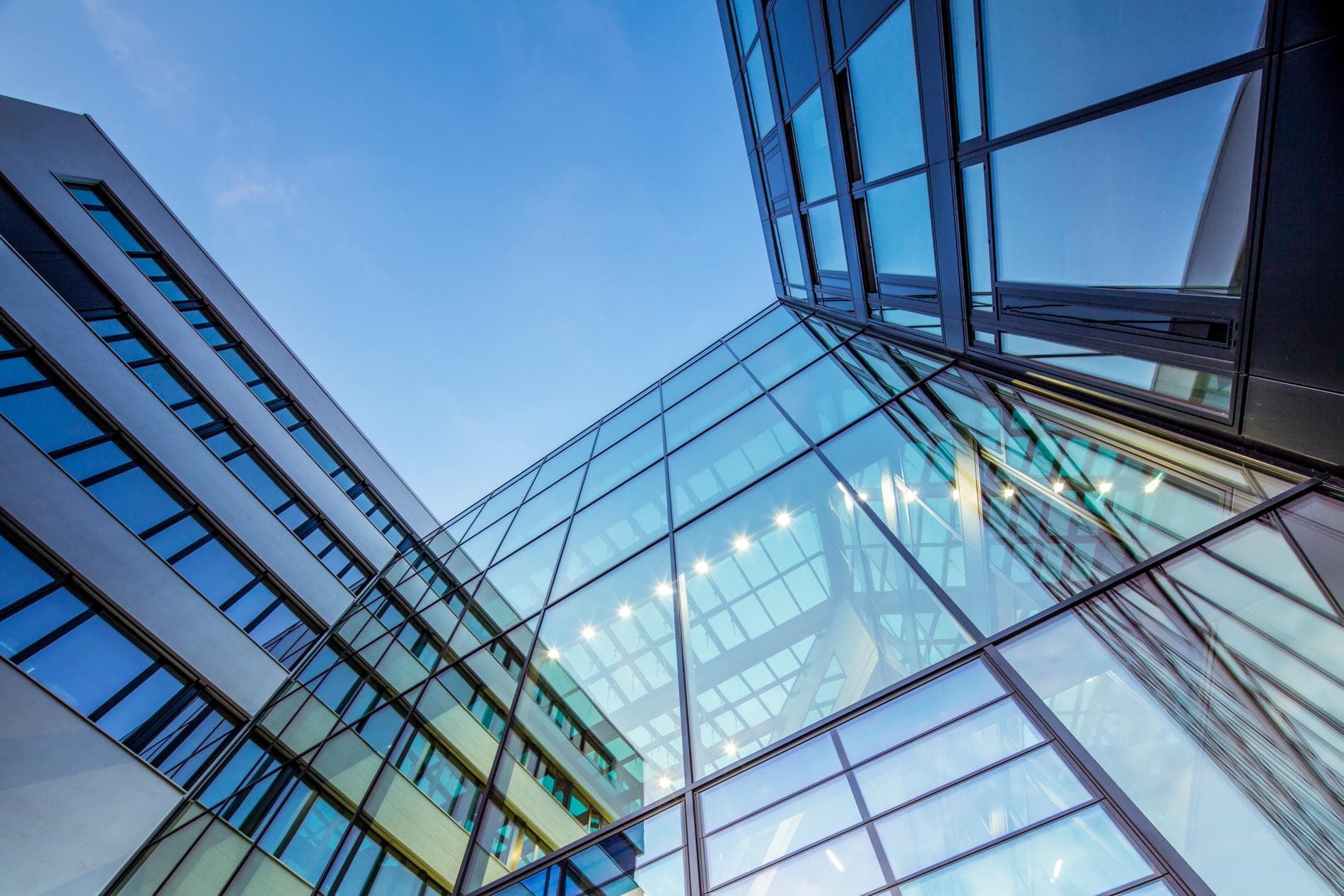 Upward view of a modern glass office building's façade against a clear blue sky