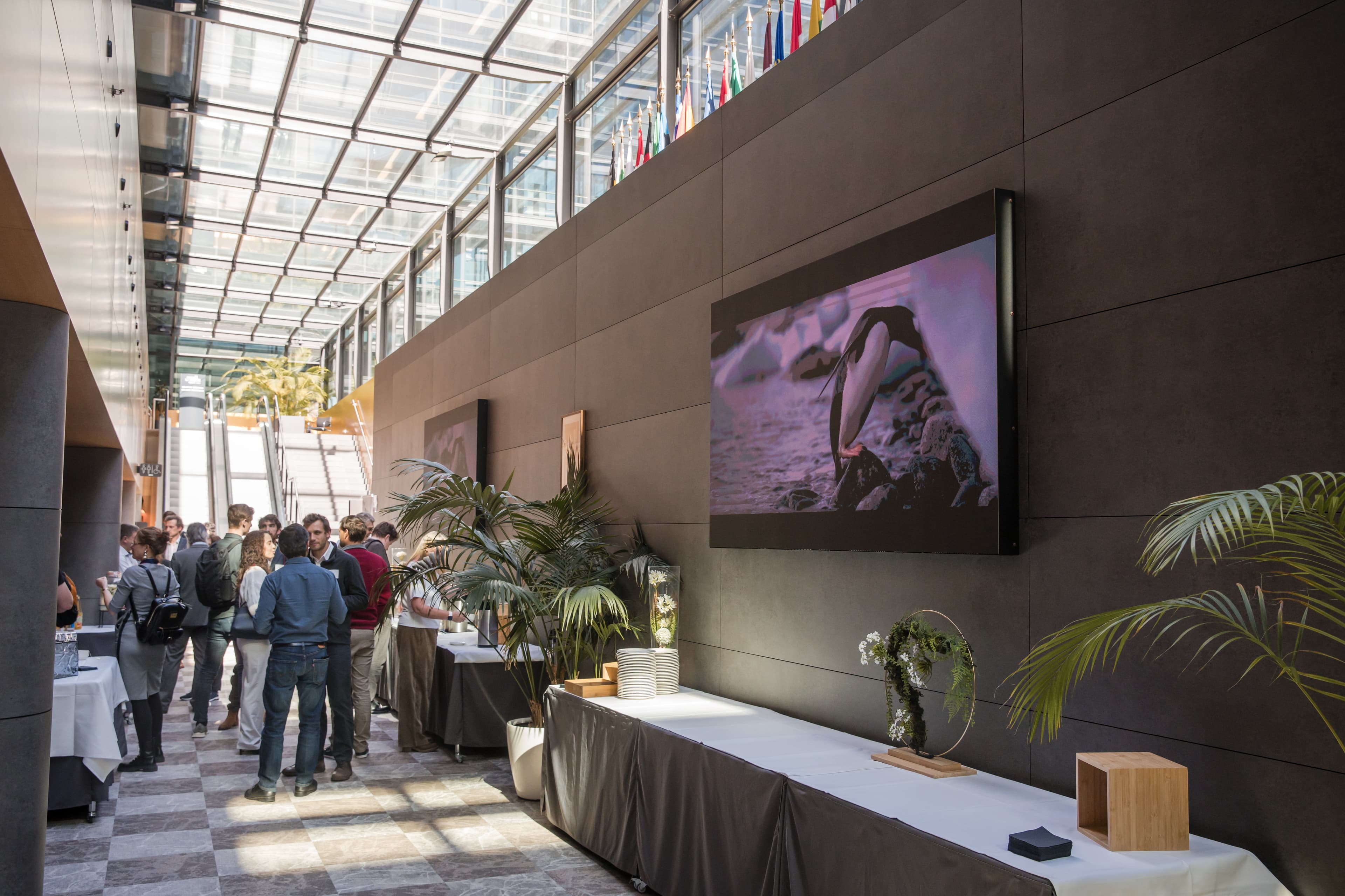 A networking break in the glass-roofed Chamber of Commerce atrium with a penguin on a screen