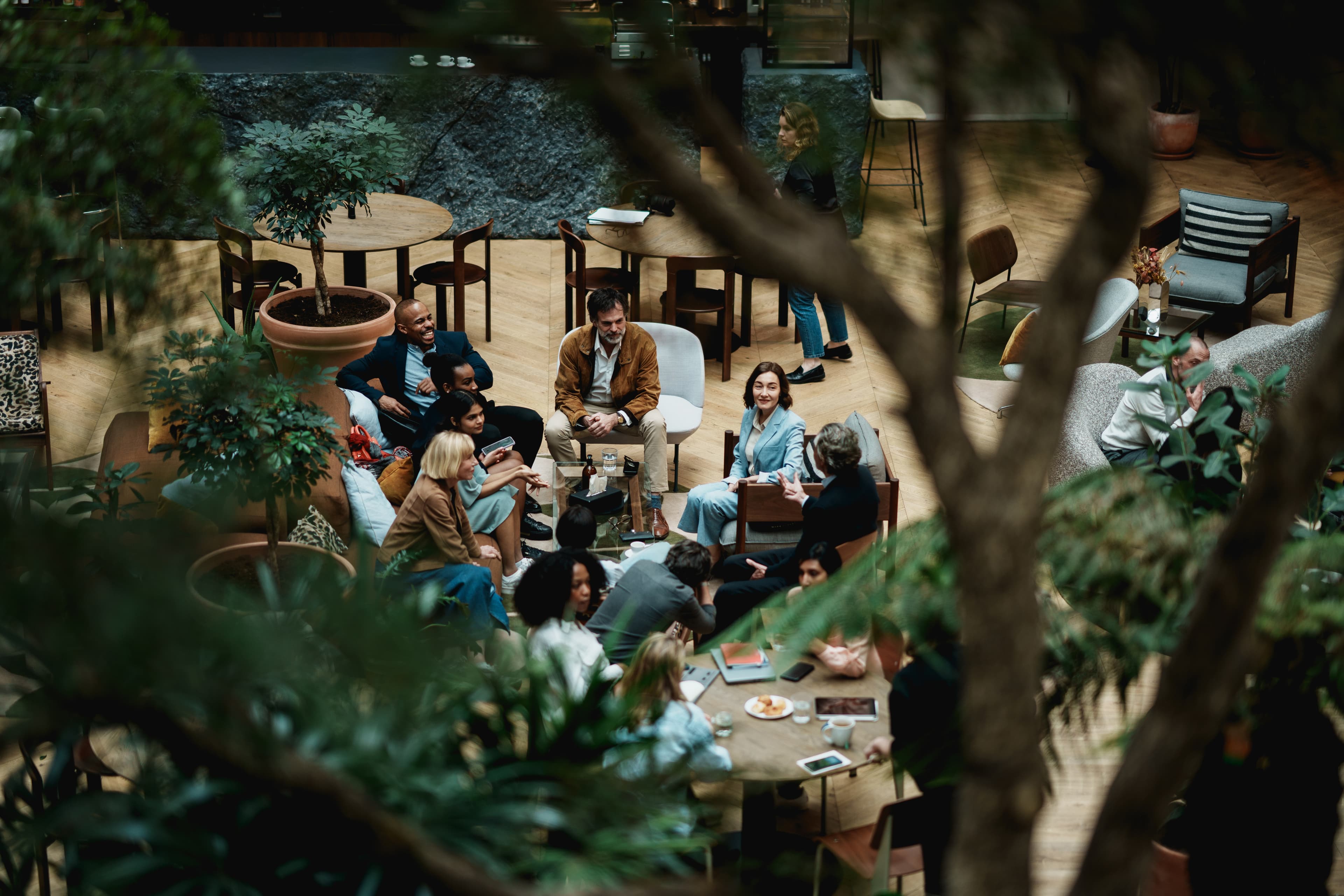 Business people gathered in a plant-filled lounge for an informal group conversation