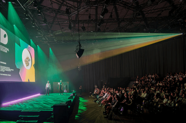 An awards ceremony on a green-lit stage before a large audience at a design awards show