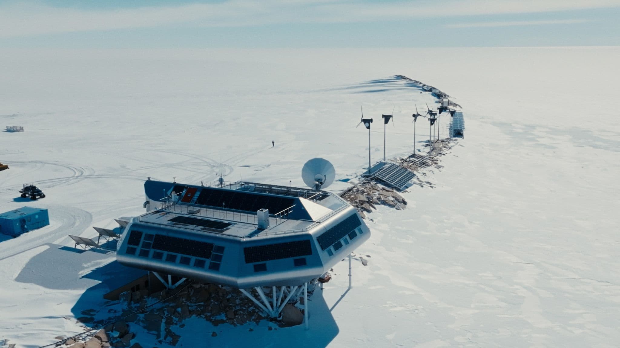 Aerial view of a polar research station on stilts with wind turbines on a snowy plain