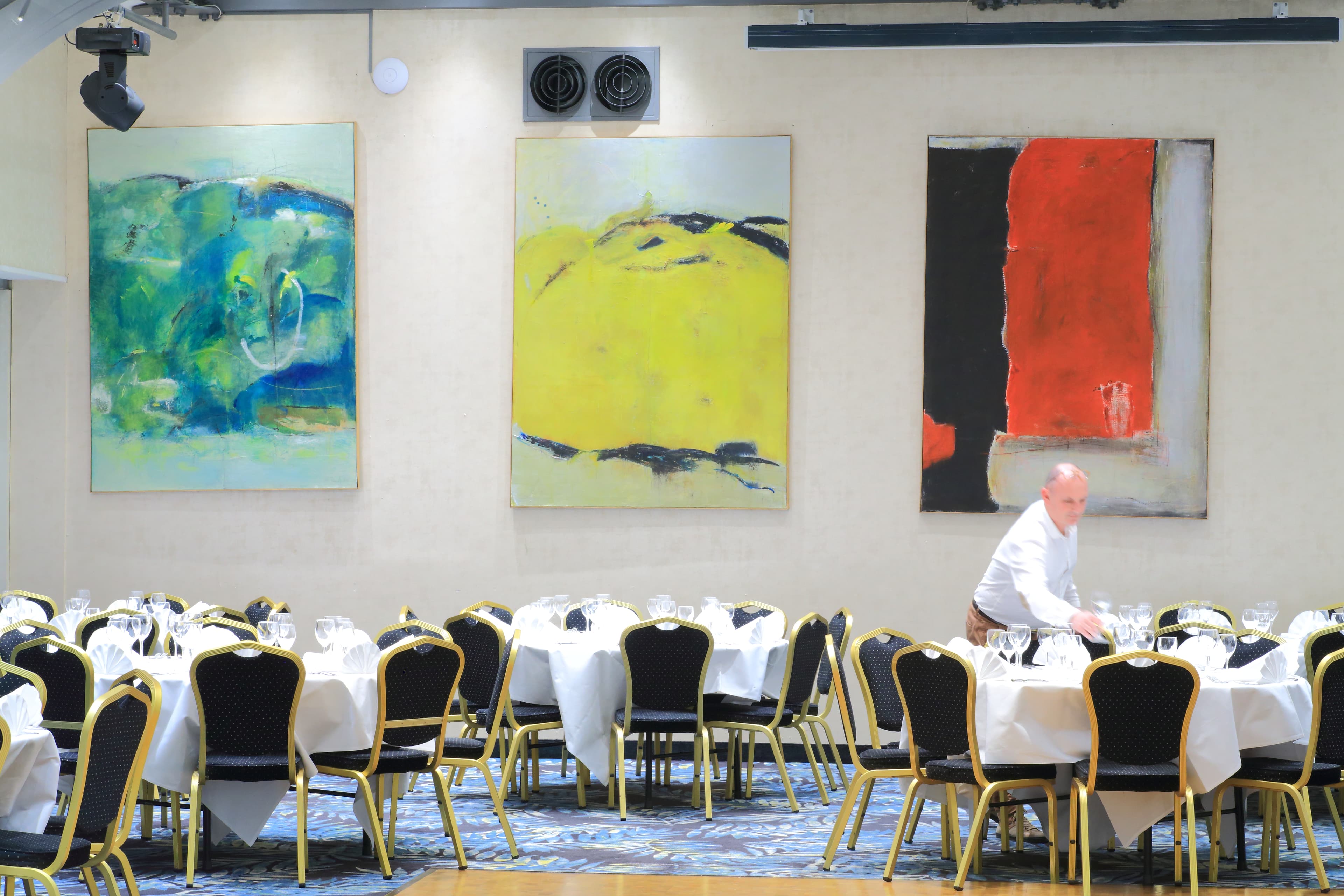 Banquet hall with set tables and modern artworks on the walls, server in action.