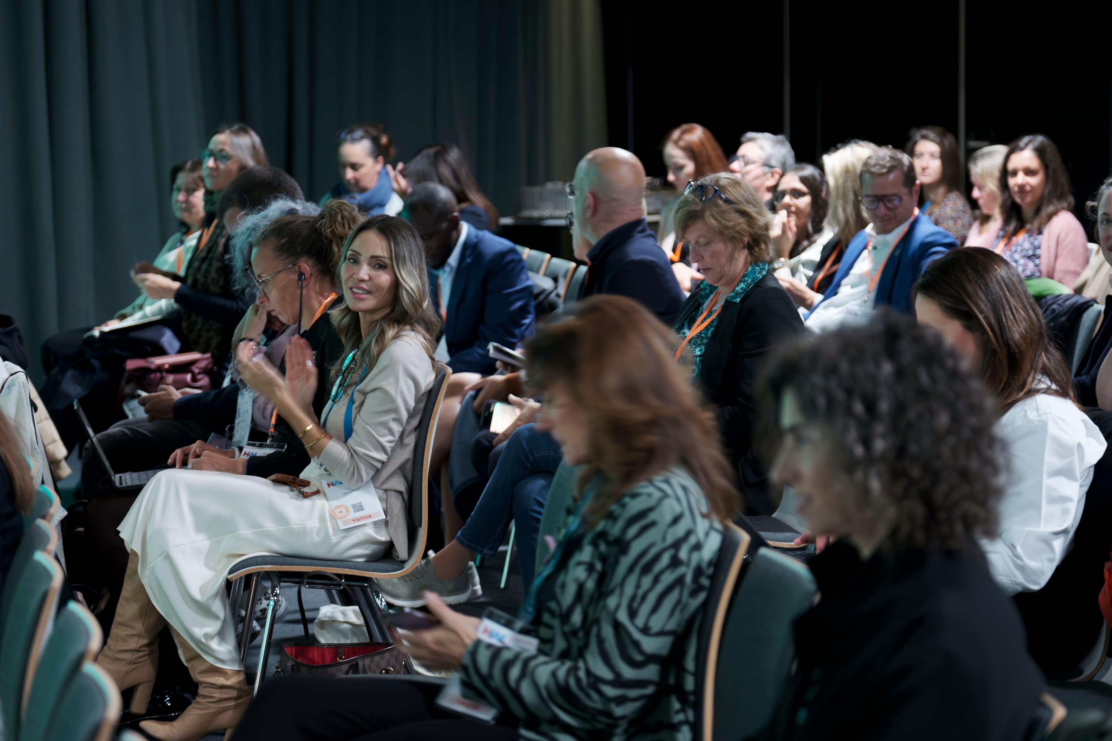 Seated audience with lanyards listening during a session at the SPX Colloquium in Luxembourg