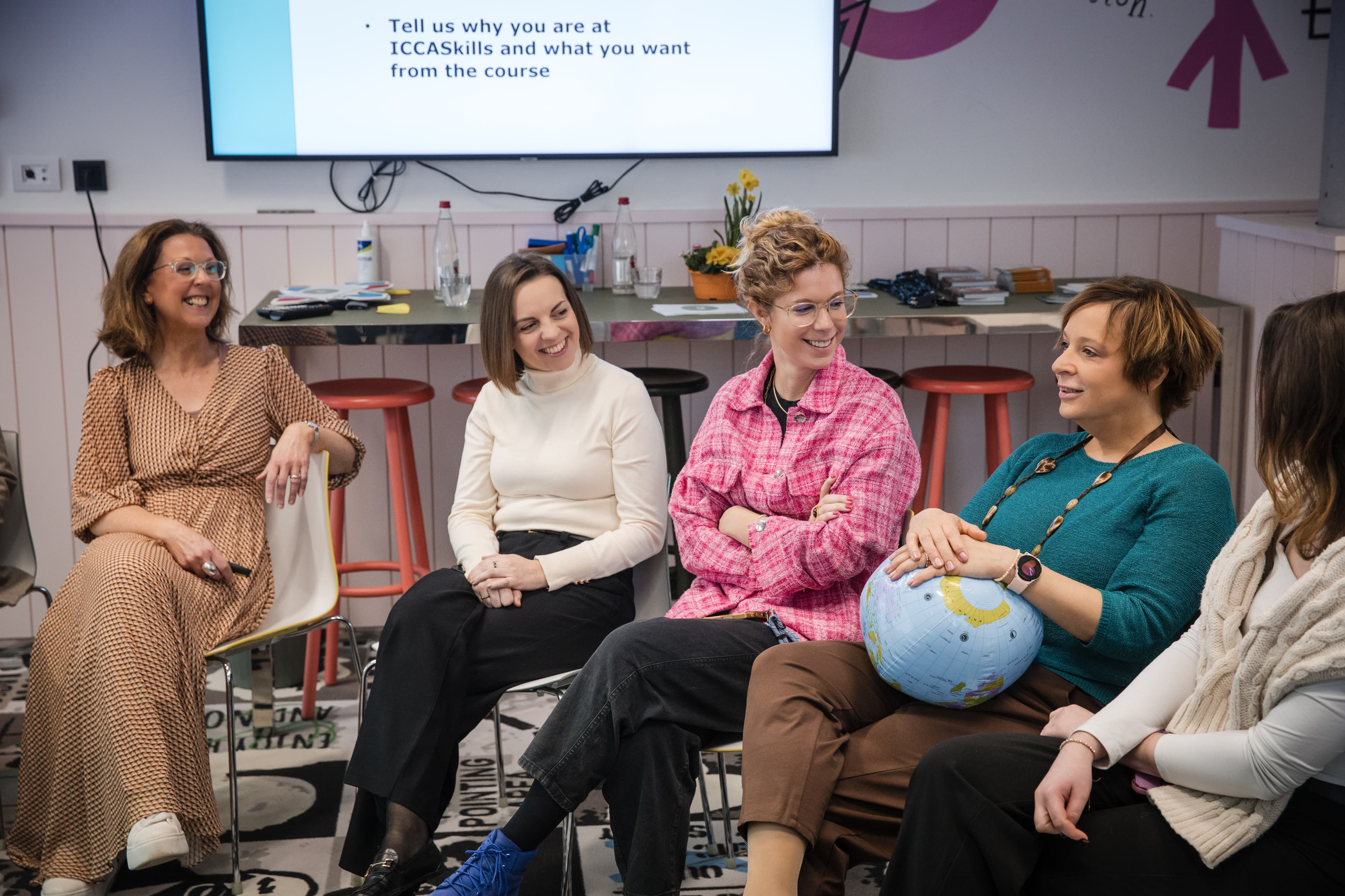 Five women laugh during an ICCA Skills course session, one holding an inflatable globe